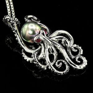 May include: A silver octopus pendant featuring a large, iridescent green pearl and two red gemstones for eyes. The octopus is intricately detailed with curled tentacles.