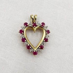 May include: A gold heart pendant, edged with small red and white gemstones. The heart shape is open in the centre. It has a small loop at the top for a chain.