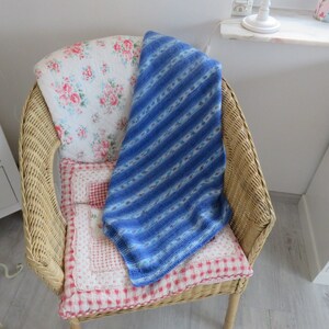 Könnte beinhalten: Ein Korbstuhl mit einer blau-weiß gestreiften Wolldecke auf einem floral gemusterten Kissen und einem rot-weiß karierten Kissen.