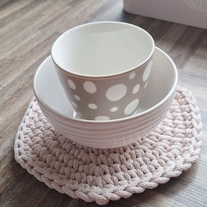Könnte beinhalten: Eine weiße Schüssel mit braunem und weißem Tupfenmuster sitzt in einer größeren weißen Schüssel. Beide Schüsseln stehen auf einem beigefarbenen gehäkelten Untersetzer.