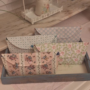 Könnte beinhalten: Vier Stoffbeutel mit floralen und geometrischen Mustern. Die Beutel sind in einem Holztablett mit blauer Lackierung angeordnet.