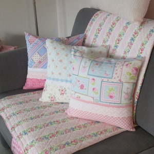 Könnte beinhalten: Ein graues Sofa mit einer pink-weißen, floral gemusterten Decke und drei Kissen. Die Kissen sind ebenfalls pink und weiß mit floralen Mustern.