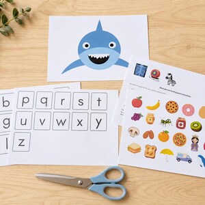 Peut inclure: Ensemble de supports p&eacute;dagogiques pour enfants, comprenant des cartes d'alphabet, une illustration de requin et un jeu d'association avec des images d'aliments. Des ciseaux bleus sont &eacute;galement pr&eacute;sents.