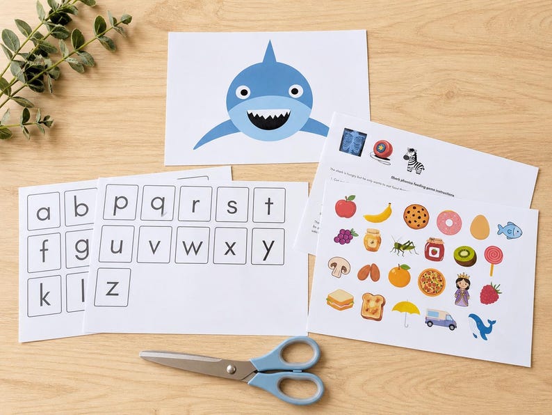 Peut inclure: Ensemble de supports p&eacute;dagogiques pour enfants, comprenant des cartes d'alphabet, une illustration de requin et un jeu d'association avec des images d'aliments. Des ciseaux bleus sont &eacute;galement pr&eacute;sents.