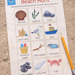 May include: A "Beach Hunt" activity sheet with illustrations of beach-related items like a seashell, seaweed, rocks, sandcastle, bird, boat, bucket and spade, driftwood, rock pool, shiny pebble, curly shell, and crab. A pencil rests on the sand next to the sheet.