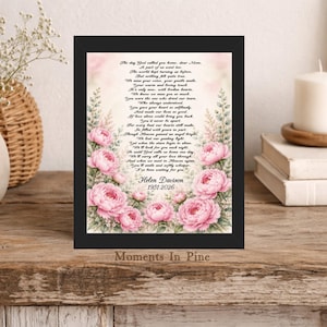 May include: A black framed memorial print featuring a poem titled The day God called you home, dear Mom, surrounded by soft pink peony illustrations. The text includes the name Helen Davison and the years 1951-2026 in a clear black font.