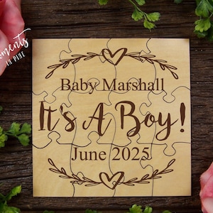 May include: Wooden puzzle piece announcement for a baby boy. The puzzle pieces are arranged to form a heart shape with the text "Baby Marshall It's A Boy! June 2025".