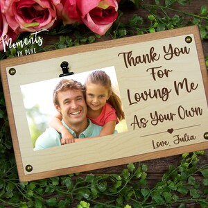 May include: A wooden photo frame with a clip at the top. The frame has a photo of a man and a girl smiling. The text on the frame reads "Thank You For Loving Me As Your Own Love, Julia".