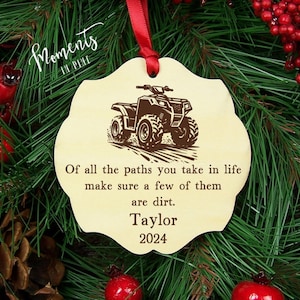 May include: A wooden Christmas ornament with a brown ATV on it. The ornament has the text "Of all the paths you take in life make sure a few of them are dirt. Taylor 2024" on it.