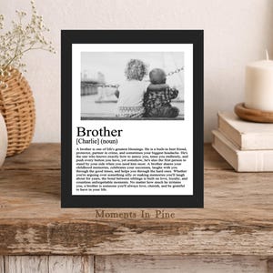 May include: A black framed print featuring a black and white photograph of two children sitting together, with the text Brother [Charlie] (noun) followed by a paragraph defining the word brother, all displayed on a white background within the frame.
