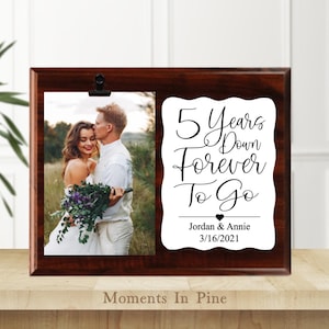 May include: A dark brown wooden photo frame with a clip holding a wedding photo. The frame has a white space with the text "5 Years Down Forever To Go" and the names Jordan & Annie with the date 3/16/2021.