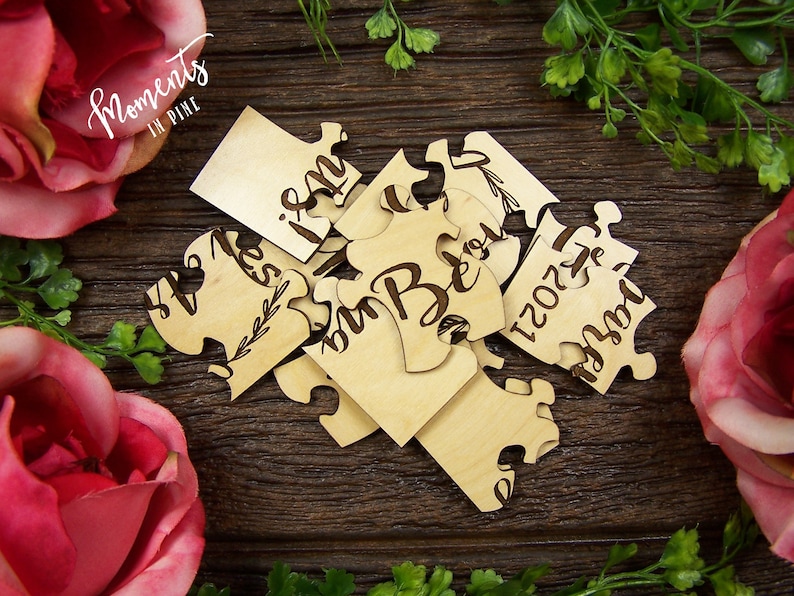 K&ouml;nnte beinhalten: Holzp Puzzle-Teile mit den Worten "We" und "Yes, I Do" sowie dem Datum "12.02.2023" eingraviert. Die Teile sind in Herzform auf einer Holzoberfl&auml;che angeordnet.