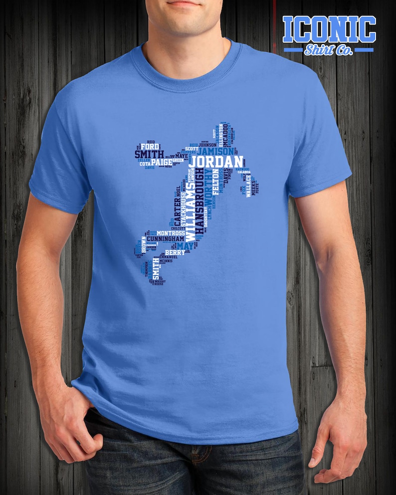 May include: A light blue t-shirt with a blue and white word cloud design in the shape of a basketball player. The word cloud includes the names of famous basketball players, such as Jordan, Smith, and Williams.