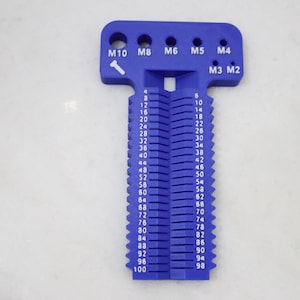 Op de afbeelding: Een blauw plastic boutmeetgereedschap met verschillende gatmaten, gemarkeerd met M10 tot M2. De tool heeft een reeks genummerde sleuven voor het meten van boutlengtes, variërend van 4 tot 100 mm.