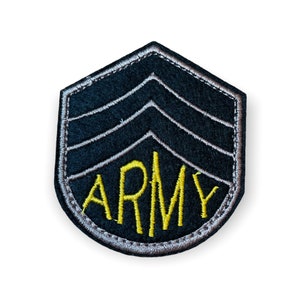 Puede incluir: Parche del Ejército de fieltro negro con tres galones y la palabra "ARMY" en amarillo. El parche tiene un borde plateado y tiene forma de escudo. Se trata de una insignia militar.