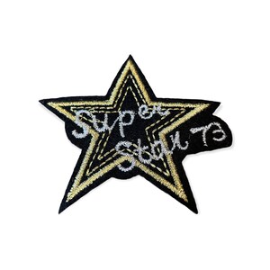 Op de afbeelding: Zwarte, stervormige patch met gouden en zilveren borduursels. De patch bevat de woorden "Super Star 73" in zilveren draad. De ster heeft een gouden omtrek en een zwart midden, perfect voor kleding of accessoires.