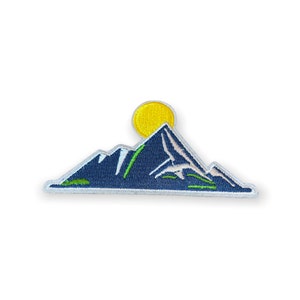 May include: Embroidered patch featuring a mountain range with a yellow sun rising behind the peaks. The mountains are navy blue with white and green accents. The patch has a white border and is likely for clothing or accessories.