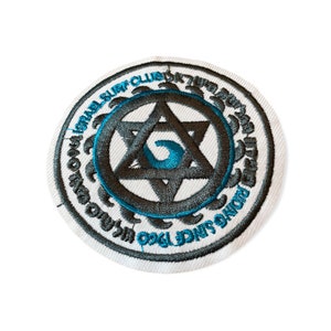 May include: Circular embroidered patch with a white background and a black and teal design. The design includes a Star of David, a wave, and text that reads "Israel Surf Club" and "Riding Since 1960".
