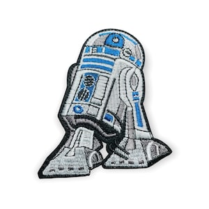 Op de afbeelding: Geborduurde patch met de iconische R2-D2 droid uit Star Wars. De patch toont een gedetailleerd ontwerp met blauwe, witte en grijze kleuren en zwarte contouren. Perfect om toe te voegen aan jassen, tassen of andere stoffen items.