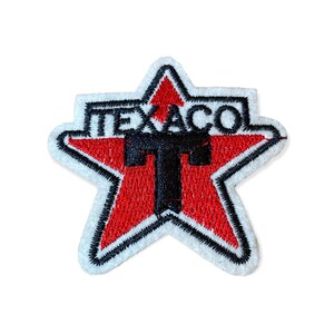 May include: Embroidered Texaco patch in the shape of a star. The star is red with a black outline and a white border. The word "TEXACO" is embroidered in white on a black background at the top, with a large black "T" in the center.