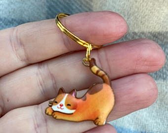 May include: A gold key chain with a cute orange and white cat charm. The cat is lying on its side with its paws outstretched.