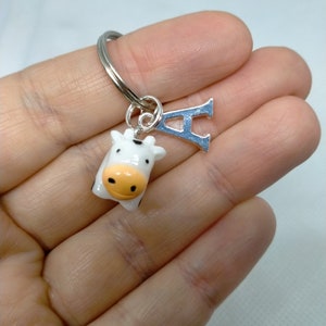 May include: A white and black cow keyring with a silver letter A charm. The cow has orange eyes and a pink nose.