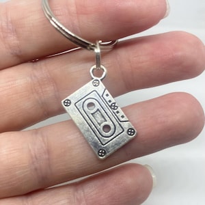 May include: Silver key chain with a silver cassette tape charm. The cassette tape charm has a detailed design with a silver ring.