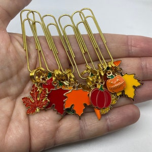 May include: A set of eight gold paper clips with autumn-themed charms. The charms include pumpkins, leaves, and acorns in shades of orange, red, and green.