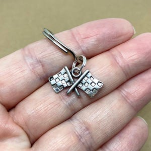 May include: Silver checkered racing flag keychain. The flags are crossed and attached to a silver key ring.