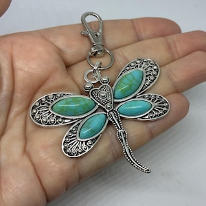 May include: Silver dragonfly keyring with turquoise stone details. The dragonfly features intricate wing patterns and a lobster clasp for secure attachment. A decorative accessory.