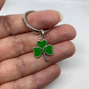 May include: A silver key ring with a green shamrock charm. The shamrock has three leaves and a silver stem.