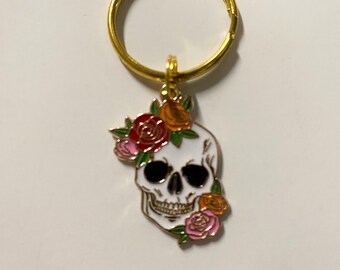 May include: A gold key chain with a white skull charm decorated with pink, red, and orange flowers.
