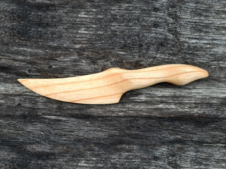 May include: A wooden butter knife with a curved handle and a pointed blade. The knife is made of light wood and has a natural finish.