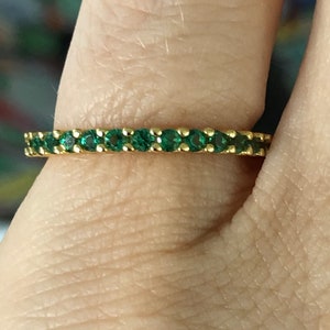 May include: A gold band ring with a row of emerald green gemstones.