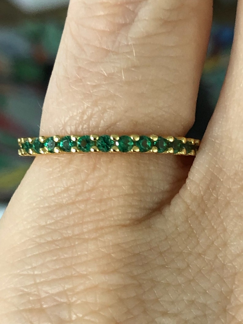 May include: A gold band ring with a row of emerald green gemstones.