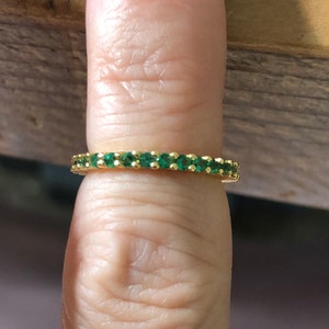 May include: A gold band ring with a row of small, emerald green stones.