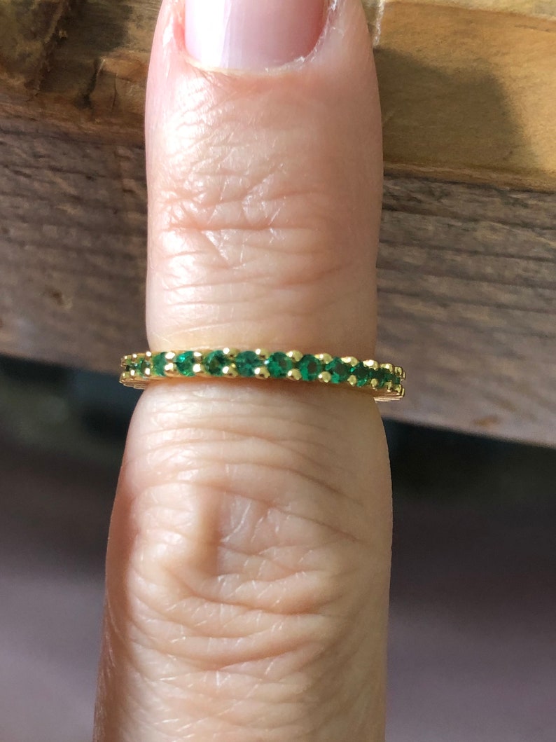 May include: A gold band ring with a row of small, emerald green stones.