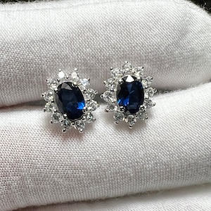 Puede incluir: Un par de pendientes de plata con una piedra ovalada azul rodeada de piedras peque&ntilde;as transparentes.