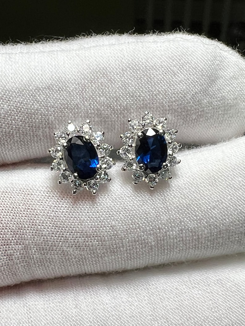 Puede incluir: Un par de pendientes de plata con una piedra ovalada azul rodeada de piedras peque&ntilde;as transparentes.