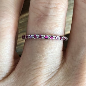 May include: A thin silver band with a row of small, bright pink gemstones.