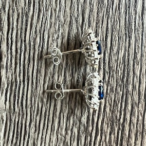 Puede incluir: Un par de pendientes de plata con una piedra preciosa azul rodeada por un halo de piedras preciosas m&aacute;s peque&ntilde;as y transparentes.