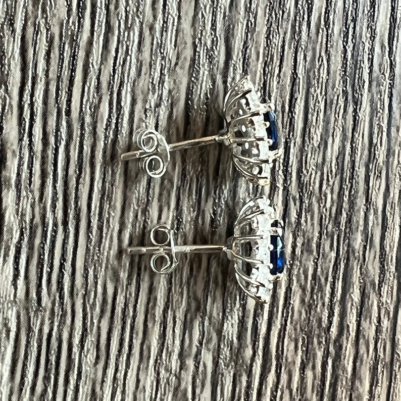 Puede incluir: Un par de pendientes de plata con una piedra preciosa azul rodeada por un halo de piedras preciosas m&aacute;s peque&ntilde;as y transparentes.