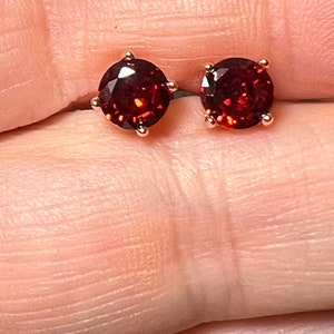 May include: A pair of rose gold stud earrings with round, red garnet gemstones.