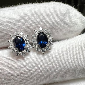 Puede incluir: Un par de pendientes de plata con una piedra ovalada azul rodeada de piedras peque&ntilde;as transparentes.