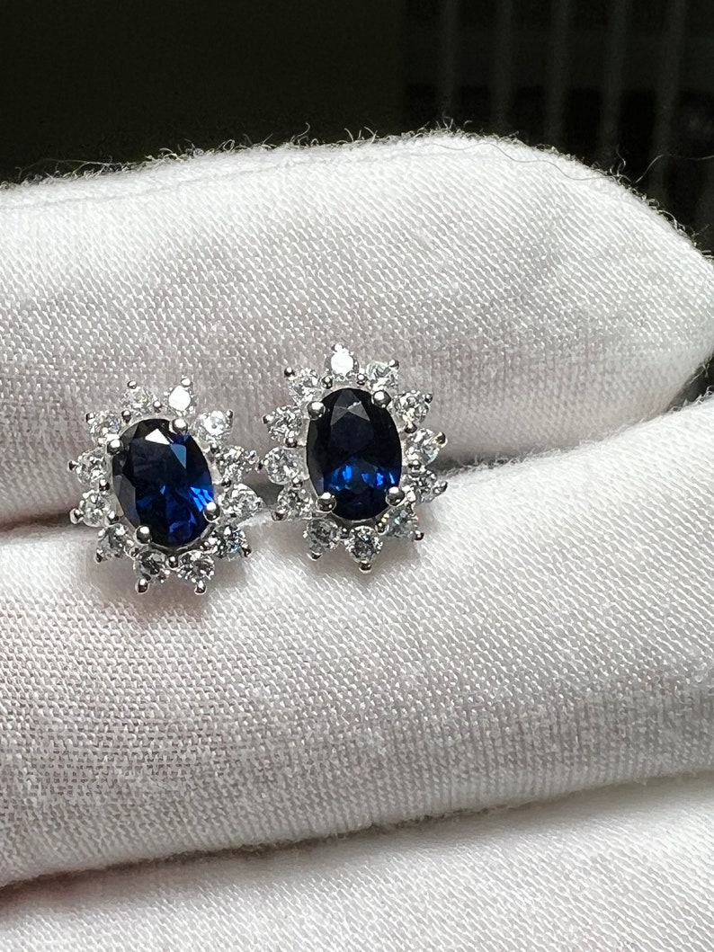 Puede incluir: Un par de pendientes de plata con una piedra ovalada azul rodeada de piedras peque&ntilde;as transparentes.