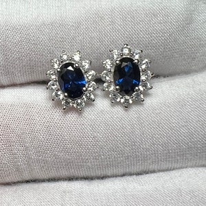 Puede incluir: Un par de pendientes de plata con una piedra ovalada azul rodeada de piedras peque&ntilde;as transparentes.