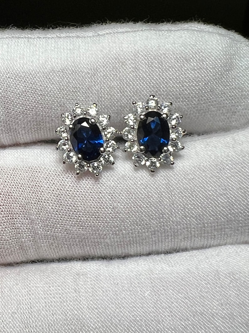 Puede incluir: Un par de pendientes de plata con una piedra ovalada azul rodeada de piedras peque&ntilde;as transparentes.