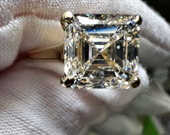 Könnte beinhalten: Ein goldener Ring mit einem großen, klaren, quadratischen Diamanten. Der Diamant ist facettiert geschliffen und in einer einfachen Fassung gefasst.