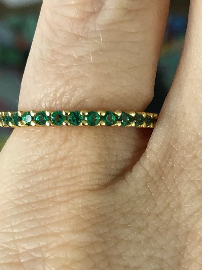 May include: A gold band ring with a row of small, green gemstones.