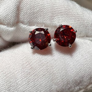 May include: A pair of silver stud earrings with round, red gemstones.